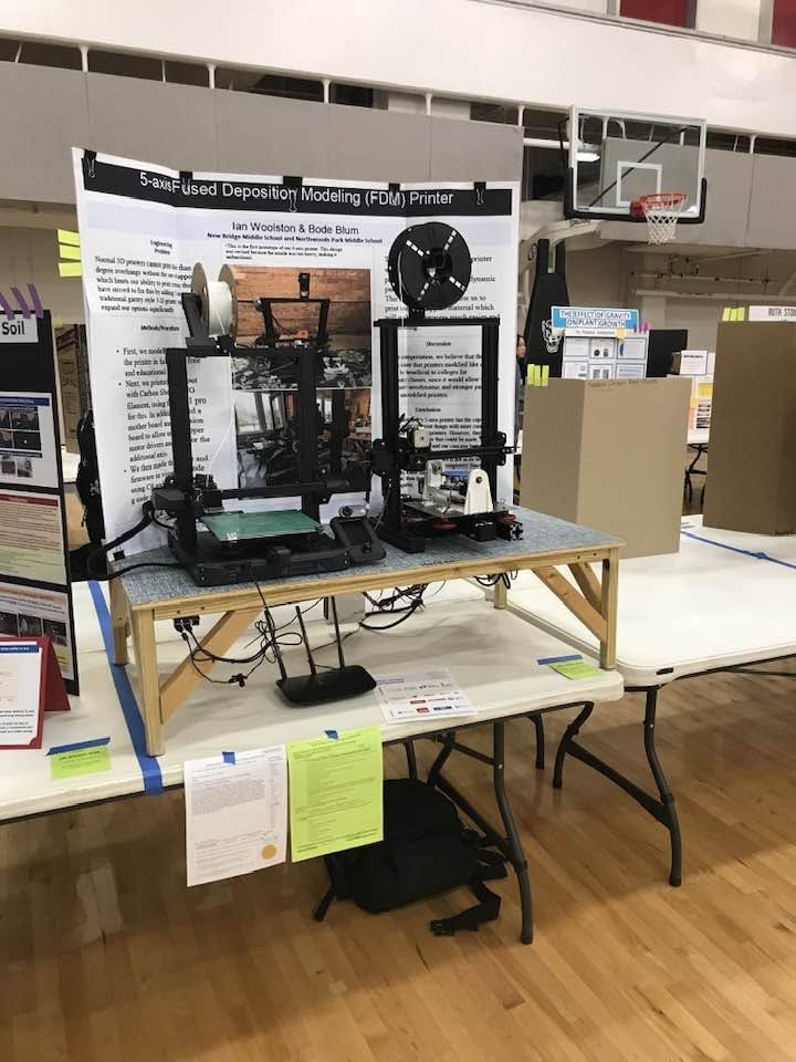 Two modified 3D printers on display at the science fair in front of the 5-axis FDM printer poster